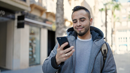 Hispanic man using smartphone smiling at street