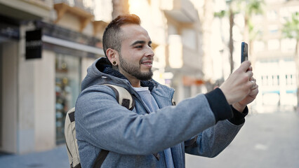 Hispanic man smiling confident taking picture with smartphone at street