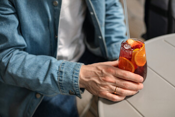 Close-up of man wearing a denim jacket drinking a summer cocktail with orange slices and strawberries