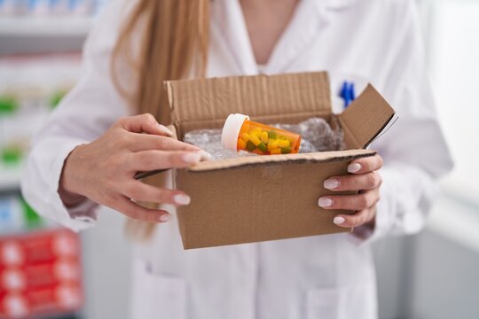 Young Caucasian Woman Pharmacist Holding Package With Pills Bottle At Pharmacy