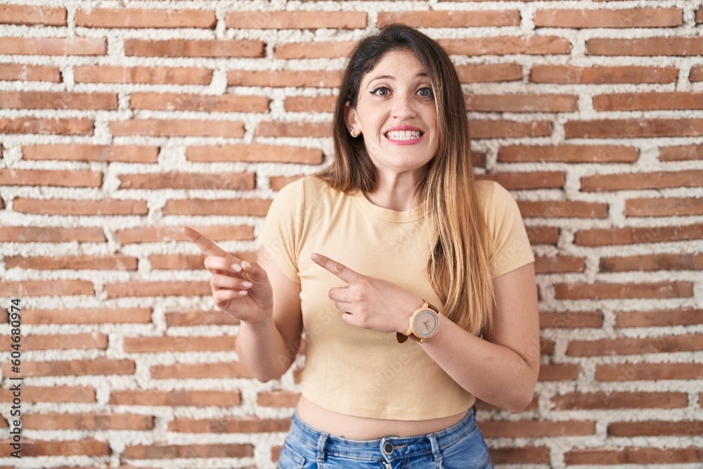 Sticker young brunette woman standing over bricks wall pointing aside worried and nervous with both hands, c