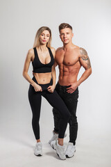 Fototapeta na wymiar Pretty happy young fashionable woman fitness model and handsome athletic muscular man with naked torso on white background. Beautiful sports couple