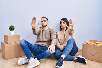 Young couple moving to a new home doing stop sing with palm of the hand. warning expression with...