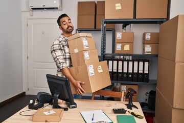 Young hispanic man ecommerce business worker holding packages at office