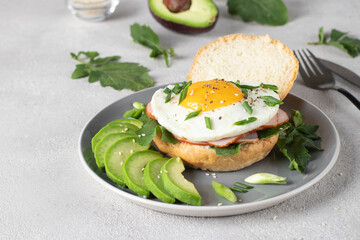 Homemade sandwich with ham, fried egg and avocado for breakfast on a gray plate