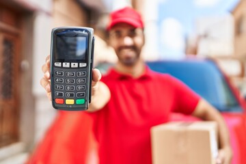 Young hispanic man courier holding package and data phone at street
