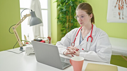 Young blonde woman doctor using laptop sitting on table at clinic