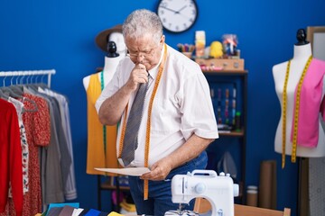 Middle age grey-haired man tailor looking clothing design at tailor shop