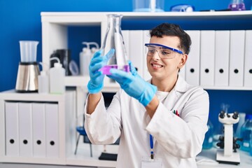 Young non binary man scientist smiling confident measuring liquid at laboratory