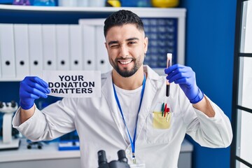 Young handsome man working at scientist laboratory holding blood sample winking looking at the...