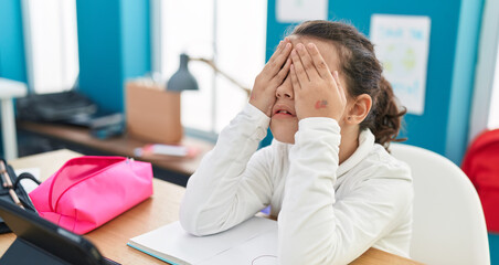 Adorable hispanic girl student stressed covering eyes with hands at classroom