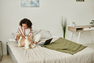 Minimal portrait of black young woman playing with cute pet dog on bed in cozy home interior, copy...
