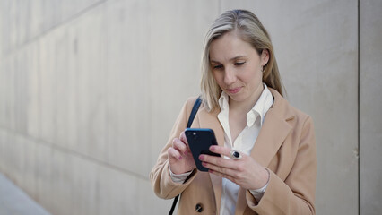 Young blonde woman using smartphone standing at street