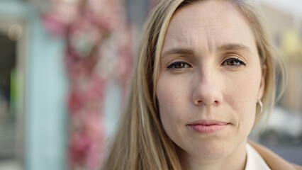 Fototapeta premium Young blonde woman standing with serious expression at coffee shop terrace