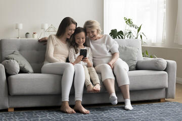 Multigenerational women family spend leisure on internet use cellphone, watch video and laugh,...