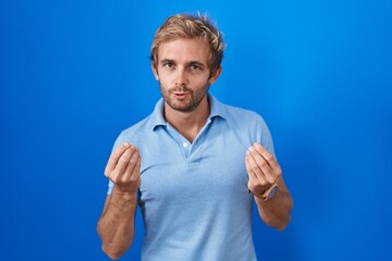 Naklejka premium Caucasian man standing over blue background doing money gesture with hands, asking for salary payment, millionaire business
