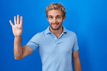 Naklejka premium Caucasian man standing over blue background showing and pointing up with fingers number four while smiling confident and happy.