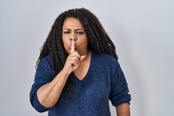 Fototapeta na wymiar Plus size hispanic woman standing over white background asking to be quiet with finger on lips. silence and secret concept.