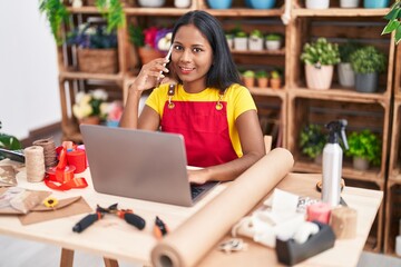 Young beautiful woman florist talking on smartphone using laptop at florist