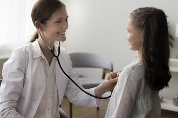Smiling attractive woman pediatrician in coat listen to little girl heart rate with stethoscope, check internal body sounds of lungs, provide professional medical help during child visit. Health-care