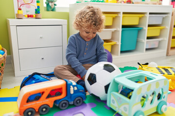 Adorable blond toddler playing with cars toy sitting on floor at kindergarten