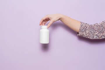 White plastic bottle in female hand in lilac background. Packaging for pills, capsules or supplements.
