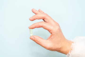 Doctor's hand holding a fish oil capsule (Omega 3) or pill isolated on light blue background