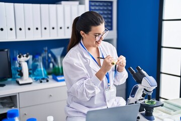 Young hispanic woman scientist write on test tube working at laboratory