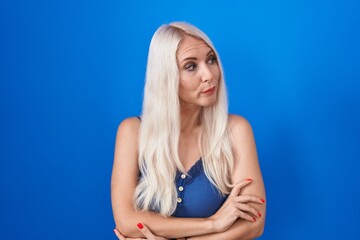 Fototapeta premium Caucasian woman standing over blue background looking to the side with arms crossed convinced and confident