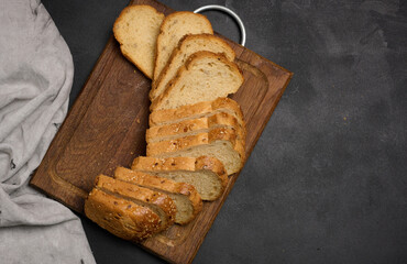 Sliced loaf of bread on a board, black table. View from above