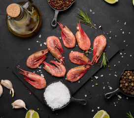 Boiled shrimp on a board, lemon slices, spices on a black background, top view