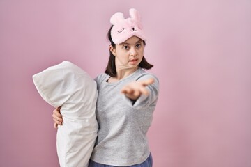 Woman with down syndrome wearing sleeping mask hugging pillow smiling cheerful offering palm hand giving assistance and acceptance.