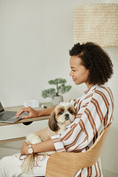 Side view portrait of black young woman working from home with pet dog sitting in lap