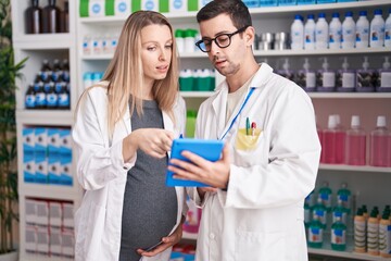 Man and woman pharmacists using touchpad speaking at pharmacy