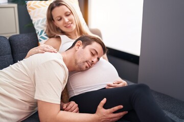 Man and woman couple listening baby sound sitting on sofa at home