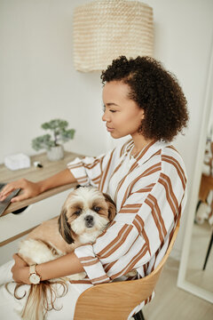 Minimal portrait of black young woman relaxing at home with pet dog sitting in lap