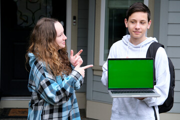 teenage boy in gray hoodie holding laptop with green screen product advertisement stern look briefcase on shoulder near his home delivery delicious food space for text free space photography