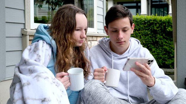 playing games on the phone drinking tea on the porch boy and girl school age fun relationship teenagers spending time together looking for something on the phone watching videos different emotions