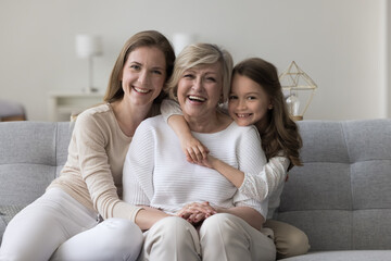 Three female generations family portrait. Cute little girl hugging tightly her beloved granny sit...