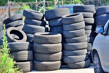 Pile of tyres near some green and a car , conceptual photo .