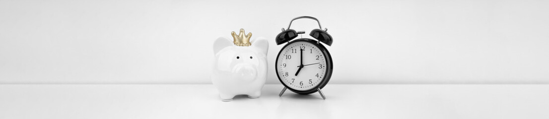 Black alarm clock with piggy bank against a white wall. Financial concept.