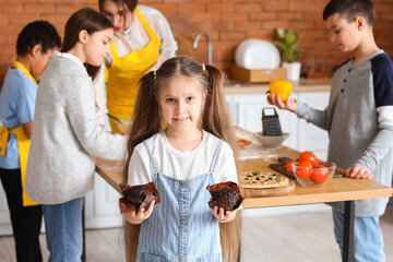 Little girl with prepared muffins after cooking class in kitchen