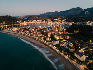 Aerial view of the city of Ribadesella at the beginning of a summer night with sea and waves on the beach at sundown hour