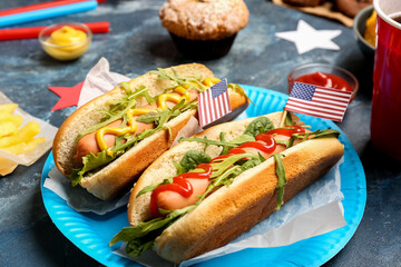 Plate of tasty hot dogs with paper American flags on color table, closeup. Memorial Day celebration