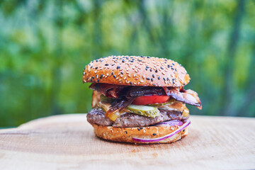 Homemade beef hamburger made from meat from organic farming and served outdoor in garden on the rustic wooden plate during hot summer sunset. Close up picture of the most popular barbeque party food.