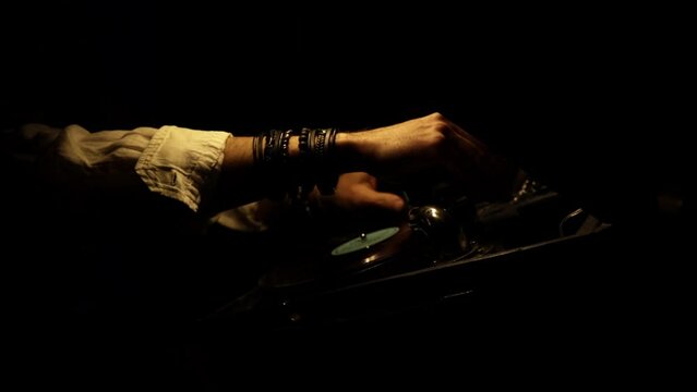 A man's hands in bracelets close-up inserting a vinyl record into an antique mechanical patiphone, putting on a needle and cranking the knob. Twilight, glare of light. High quality FullHD footage