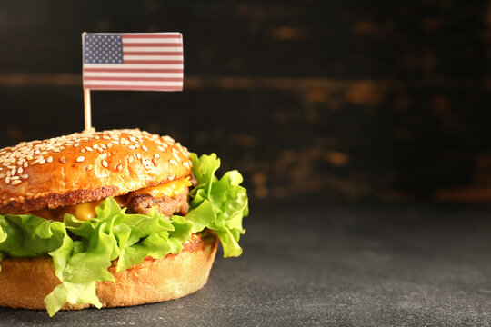 Tasty burger with paper American flag for Memorial Day celebration on dark background