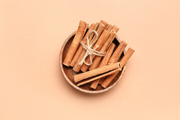 Wooden bowl with cinnamon sticks on color background
