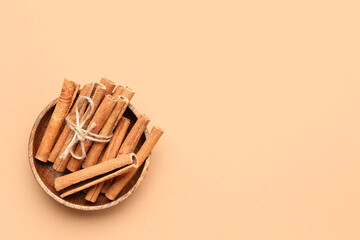 Wooden bowl with cinnamon sticks on color background