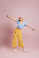 Full length of fashionable young woman dancing and smiling against color background